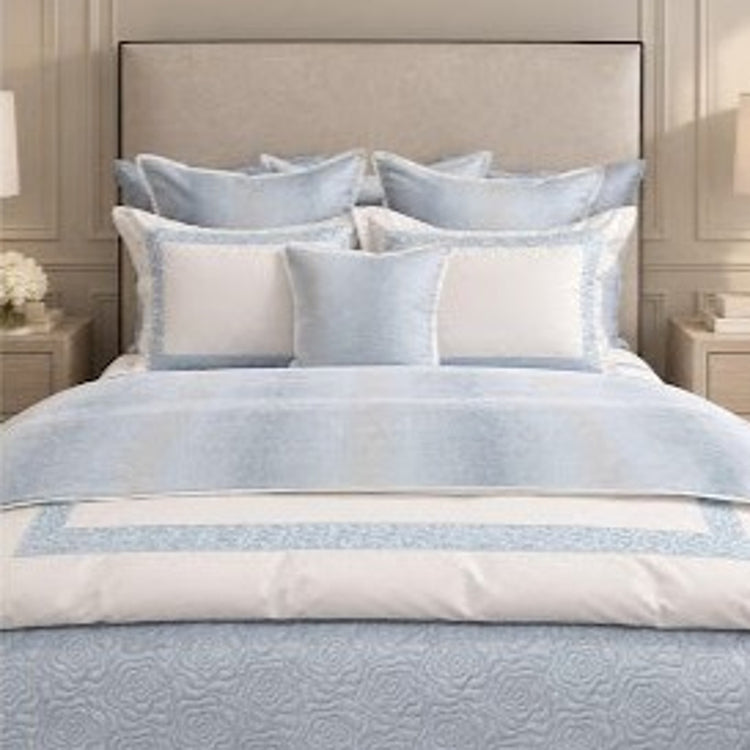 A light blue and white bedding set displayed on a bed, featuring a textured duvet cover, matching pillow shams, and solid white accent pillows in a bedroom setting.