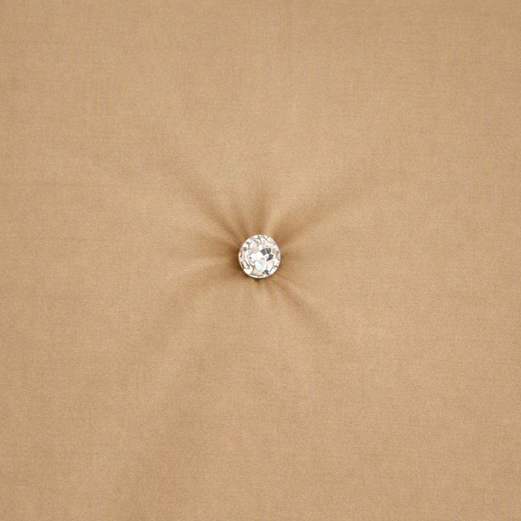 A single round clear crystal or gemstone stud with a silver-toned setting, centered on a soft, sandy beige fabric background. Swatch of Monaco Crystal in Sand - COMOK-SAN-IVO COMOQ-SAN-IVO THMOK-SAN-IVO