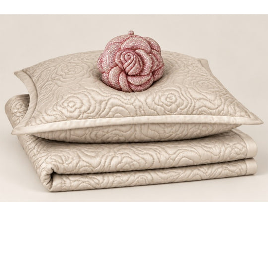 A product silo of the Roses Coverlet Set from Judith Leiber Couture by Ann Gish, shown in Bone, featuring the signature rose‑quilted coverlet with matching shams and topped with a Judith Leiber Rose clutch. - YSETCORQK‑BLE YSETCORQQ‑BLE